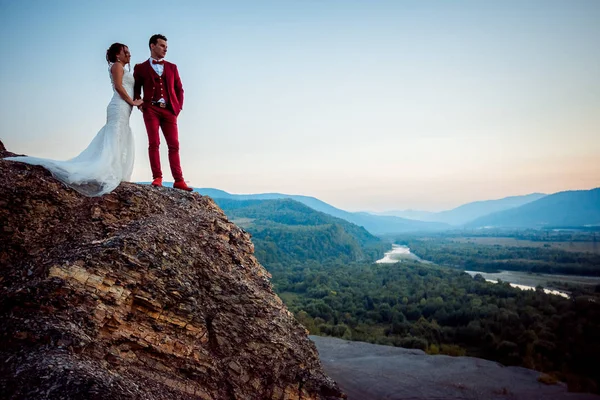 户外肖像美丽时尚新婚夫妇牵手站立的山岩石风景河森林日落享受自然. — 图库照片