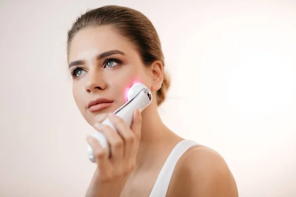 Doğal makyaj elektrik yüz masajı izole beyaz arka plan kullanarak sağlıklı taze Bayan.