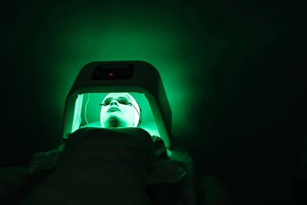 Молодая женщина в очках маски и солярия отдыхает в солярии с зеленым светом в салоне красоты. Концепция ухода за кожей . — стоковое фото