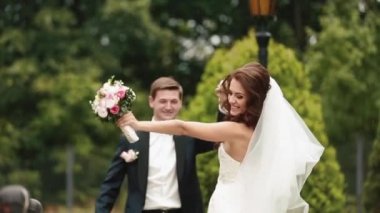 Thecheerful güzel yeni evli çiftin gülümseyerek elele ve yeşil çiçek Bahçe boyunca yağmurda yürümek.