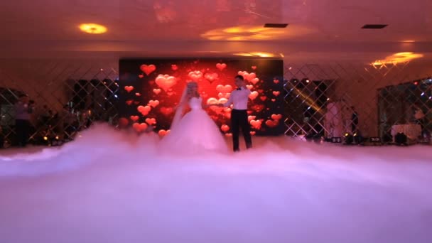 El primer baile de los recién casados felices con estilo en el restaurante en el fondo de la pantalla de visualización con corazones. Pareja está envuelta por el humo blanco . — Vídeos de Stock