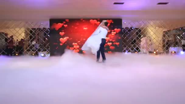Lo sposo bello sta girando intorno alla sua sposa affascinante mentre balla il loro primo ballo nel salone del ristorante coperto di fumo bianco denso . — Video Stock
