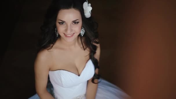 La joven hermosa novia con pelo rizado oscuro decorado con orquídeas y maquillaje natural es encantadora sonriendo mientras mira en la cámara . — Vídeo de stock