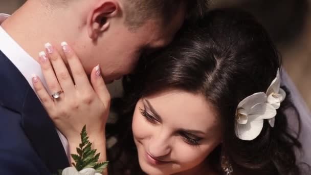 Érzékeny közeli lövés a átölelve newlywed pár. A bájos mától natúr smink és göndör haj díszített orchideák gyengéden megsimogatta az arcát kedvese. — Stock videók