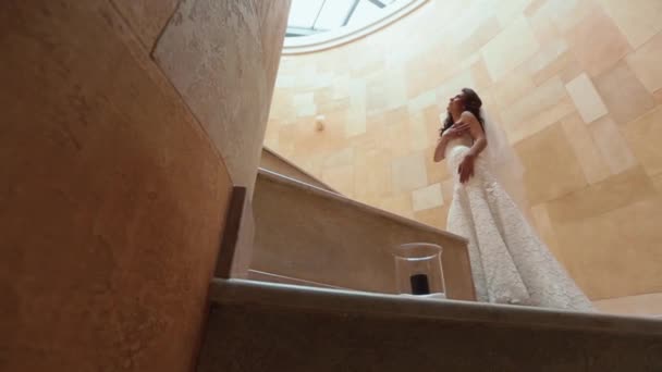 Красива молода наречена з чорним довгим кучерявим волоссям і стильним весільним платтям позує на жовтих сходах. Вид на свічку на підлозі . — стокове відео