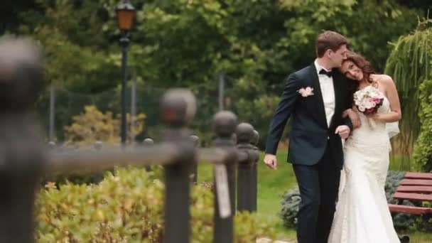 Свадебный снимок красивой счастливой пары, улыбающейся и нежно целующейся во время прогулки по зеленому цветущему саду . — стоковое видео