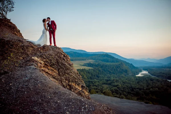 Beijar recém-casados à beira das montanhas. Retrato sensível durante o pôr-do-sol. Bela natureza . — Fotografia de Stock