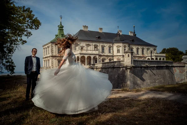 Die bezaubernde Braut tanzt und dreht sich in der Nähe des hübschen Bräutigams im Hintergrund des alten Schlosses. — Stockfoto