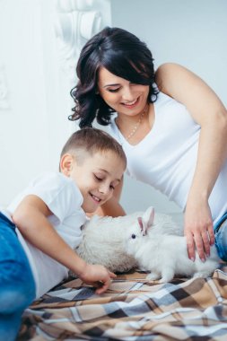 Mutlu gülümseyen anne ve ekose evde yalan güzel kabarık tavşan ile oynayan sevimli küçük sarışın oğlu aile portresi.