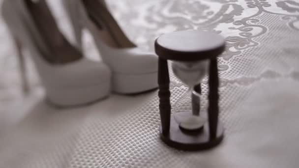 Vista de cerca de la composición de la boda que consiste en el reloj de arena vintage de pie detrás de los tacones altos blancos . — Vídeos de Stock