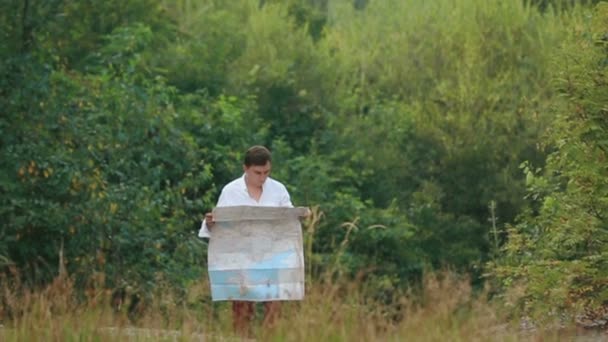 Il viaggiatore smarrito tiene la mappa e vaga lungo la foresta tra le montagne. Vista drone . — Video Stock