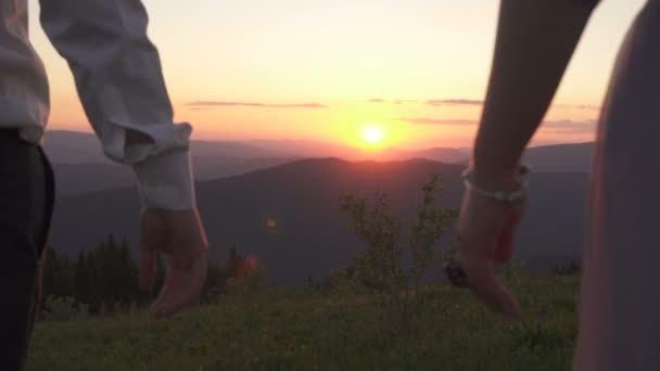 Vue rapprochée du couple tenant la main à l'arrière-plan du coucher de soleil dans les montagnes. Ils se donnent la main. 4k — Video