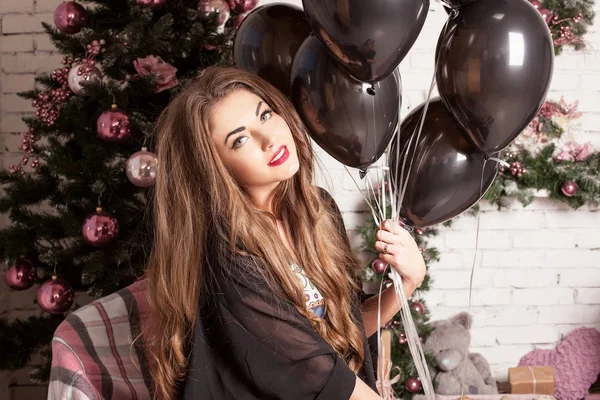 Nahaufnahme einer hübschen jungen Frau mit hübschem Make-up und langen Haaren, die ein Bündel Luftballons in der Hand hält. Weihnachtsdekoration auf einem Hintergrund. — Stockfoto