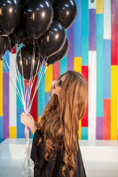 Langharige meisje met een bundel van baloons poseren voor de camera op een kleurrijke achtergrond. — Stockfoto