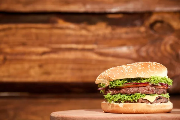 Великий, смачний, соковитий і свіжий бургер з м'ясом, овочами і листям салату, розміщеним на дерев'яній дошці . — стокове фото