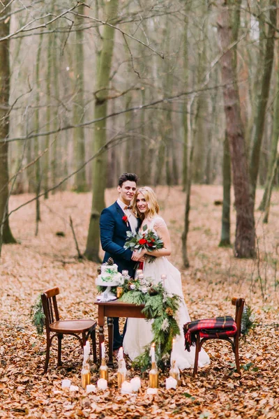 Hermosa pareja de boda posando cerca de la mesa vintage en el bosque de otoño — Foto de Stock