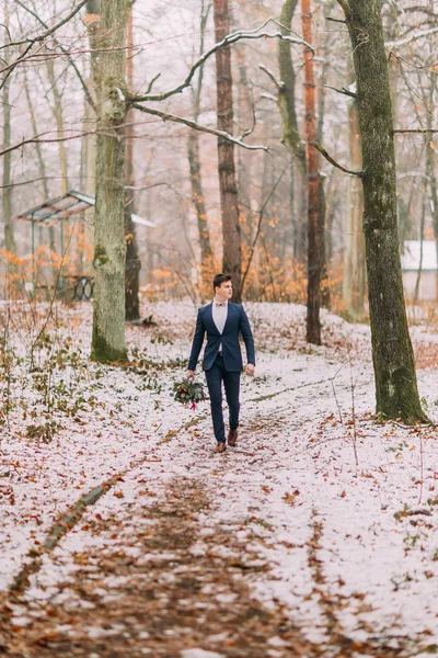 Bonito noivo com buquê em mãos caminha na floresta de outono — Fotografia de Stock