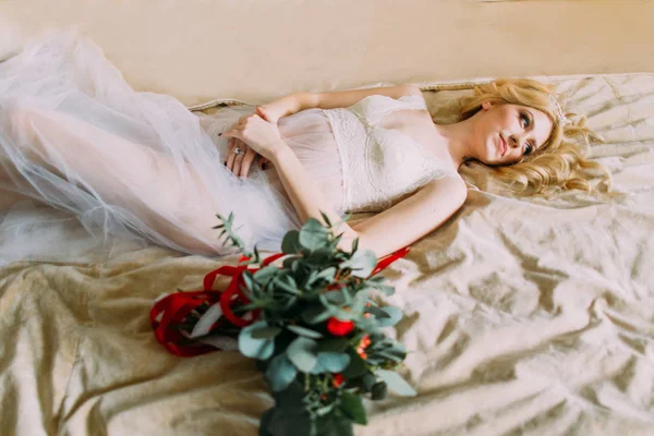 Hermosa novia rubia en ropa interior blanca, ramo de rosas rojas en primer plano. Dormitorio . — Foto de Stock