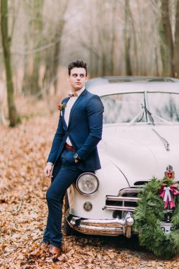 Yakışıklı şık damat sonbahar ormandaki eski model araba yakın duran