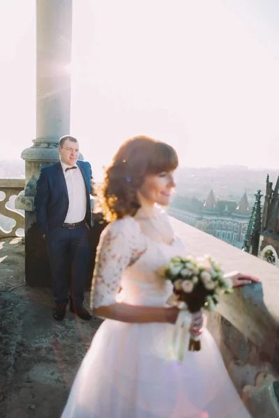 Cheerful bride and her loving new husband posing on the balcony of old gothic cathedral — Stock Photo, Image