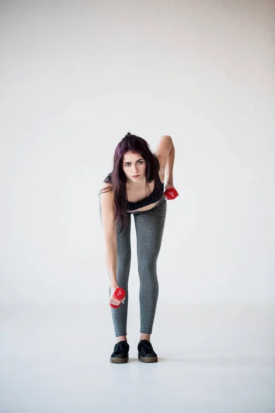Serious sportwoman is doing hand exercises with dumbbells in the studio. Full-length front view. — Stock Photo, Image