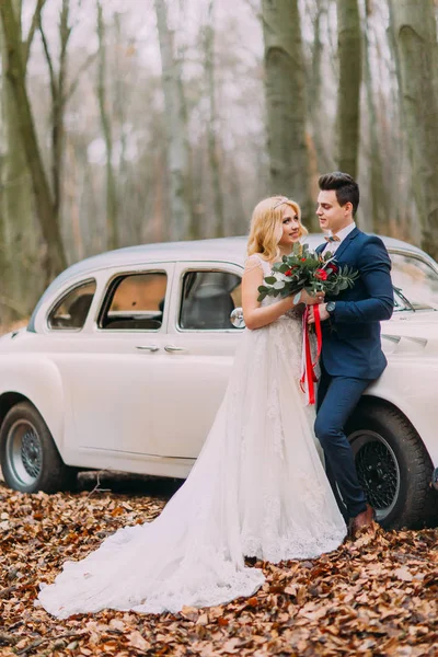 Hermosa pareja de boda posando cerca del coche en el bosque — Foto de Stock