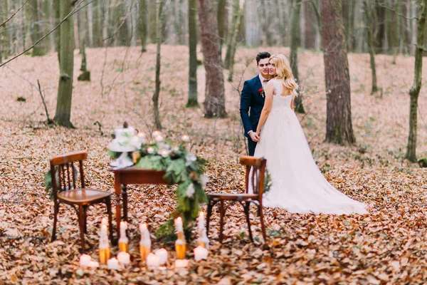 Hermosa pareja de boda tomados de la mano cerca de la mesa vintage en el bosque de otoño — Foto de Stock