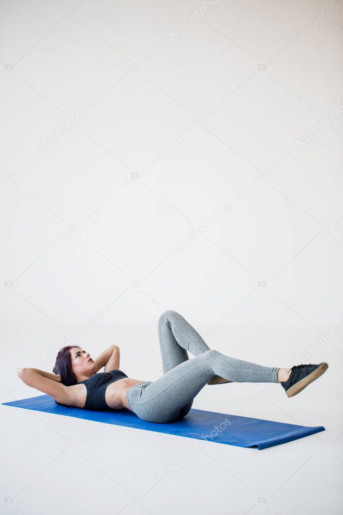 Sport tutorials for beginners to warm up. The attractive athletic trainer is lying on the mat and doing bicycle crunches in the white studio.