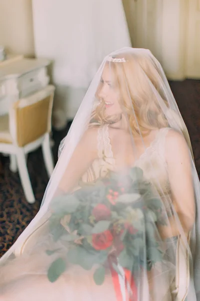 Сексуальная блондинка-невеста держит букет, одетый только в вуаль и белое белье — стоковое фото