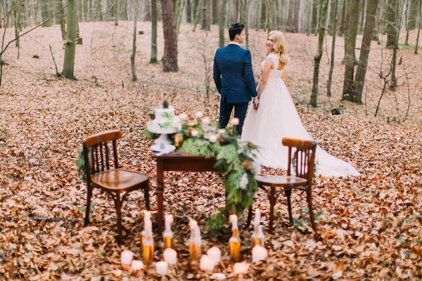 Hermosa pareja de boda tomados de la mano cerca de la mesa vintage en el bosque de otoño — Foto de Stock