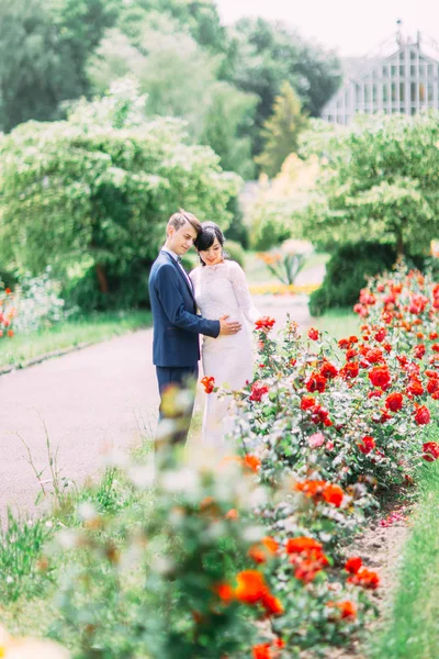 Είστε βλέποντας οι νεόνυμφοι αγκαλιάζει τα κόκκινα λουλούδια στο πάρκο. — Φωτογραφία Αρχείου