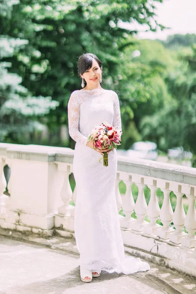 Повнометражний вигляд щасливої нареченої, що тримає весільний букет біля паркану . — стокове фото