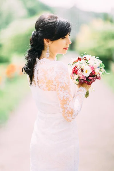Sida porträttet av den vackra bruden i spetsklänning holding den färgglada brudbukett. — Stockfoto