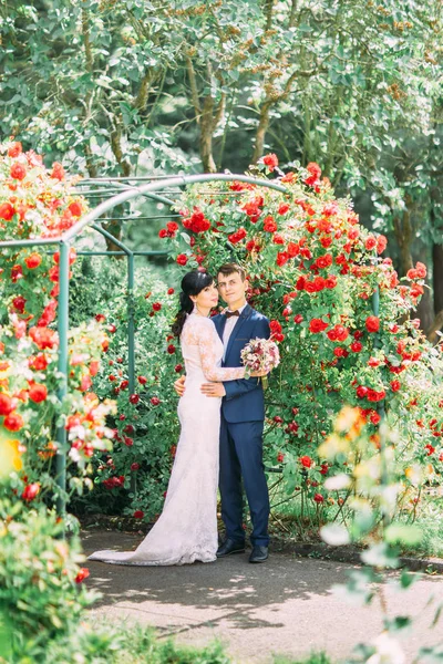 Abraçando recém-casados estão gastando seu tempo no jardim de rosas . — Fotografia de Stock