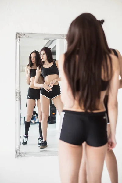 Reflexión en el espejo de dos jóvenes mujeres deportivas atractivas mirando a un lado en el gimnasio moderno . — Foto de Stock
