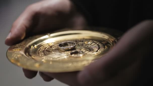 Чоловічі руки тримають золоту тарілку з обручками під час церемонії в церкві . — стокове відео