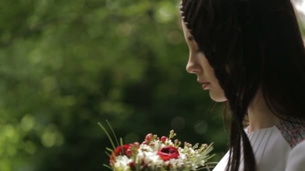 Retrato lateral de la hermosa morena joven en tela bordada está oliendo el ramo de flores al aire libre . — Vídeos de Stock
