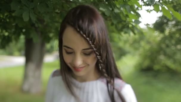 Jonge aantrekkelijke vrouw met mooie glimlach is een wandeling langs het groene park. De brunette draagt de jurk borduurwerk. — Stockvideo