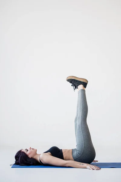 Tutorial untuk pemula olahraga. Wanita kebugaran muda berbaring di tikar dan mengangkat kakinya di studio putih . — Stok Foto