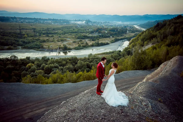 全长浪漫的户外肖像美丽幸福新婚夫妇牵手在岩石的边缘在河和森林的背景. — 图库照片