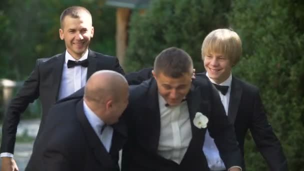 Retrato del novio feliz divirtiéndose con sus tres mejores hombres mientras camina por el parque . — Vídeo de stock