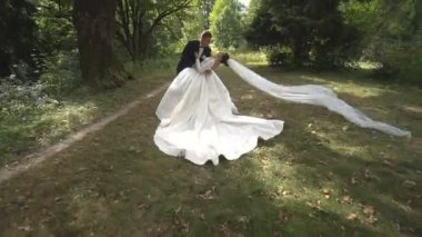 Kamera mutlu şık yeni evli çift ormanda sarılma etrafında çember. Gelin peçe gelen Rüzgar hareket ediyor.