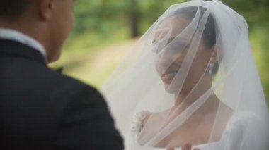 Damat gülümseyen güzel esmer gelin peçe parkta kaldırma. Omzunun üzerinden görüntüleyin. Yakın çekim.