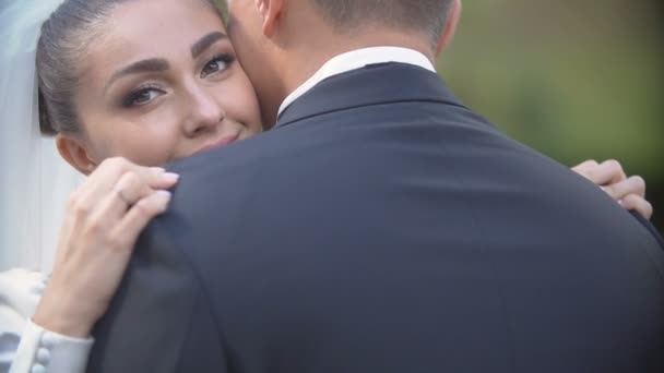 Uitzicht over bruidegom schouder naar de mooie charmante brunette bruid glimlachend en teder knuffelen haar minnaar buiten. — Stockvideo