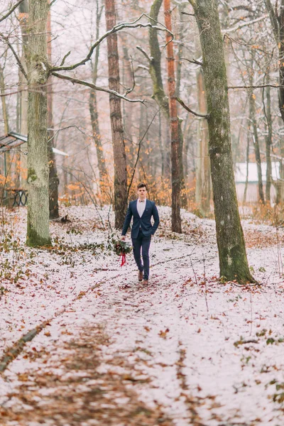 Stilig brudgummen med bukett i händer promenader på hösten skogen — Stockfoto