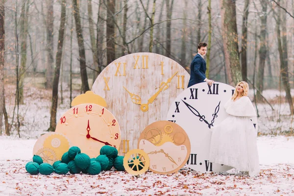 Feliz pareja de boda posando en los grandes relojes vintage en el bosque de otoño. Decoraciones creativas — Foto de Stock