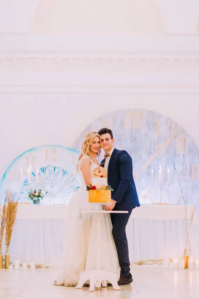 Casamento casal sorrindo e posando para câmera. Bolo doce em primeiro plano — Fotografia de Stock