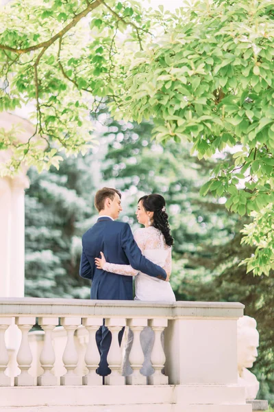 La vista trasera de la pareja recién casada abrazada detrás de la vieja valla . — Foto de Stock