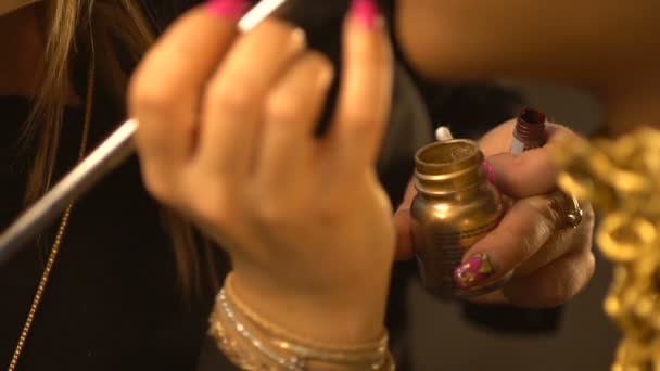 De professionele make-up artiest is het toepassen van de gouden glanzend lippenstift met behulp van de borstel op het gezicht van Afro-Amerikaanse model. Close-up beeld van de handen. — Stockvideo