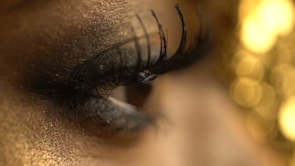 Female blinking eye of the african woman covered with golden eyeshadows and eyeliner. Close-up view. Make-up and fashion concept. — Stock Video